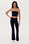 A person with long hair in a long braid stands against a plain background wearing the SPLITS59 Hazel Airweight Crop Bandeau - Black, black flared spandex pants, and white shoes.