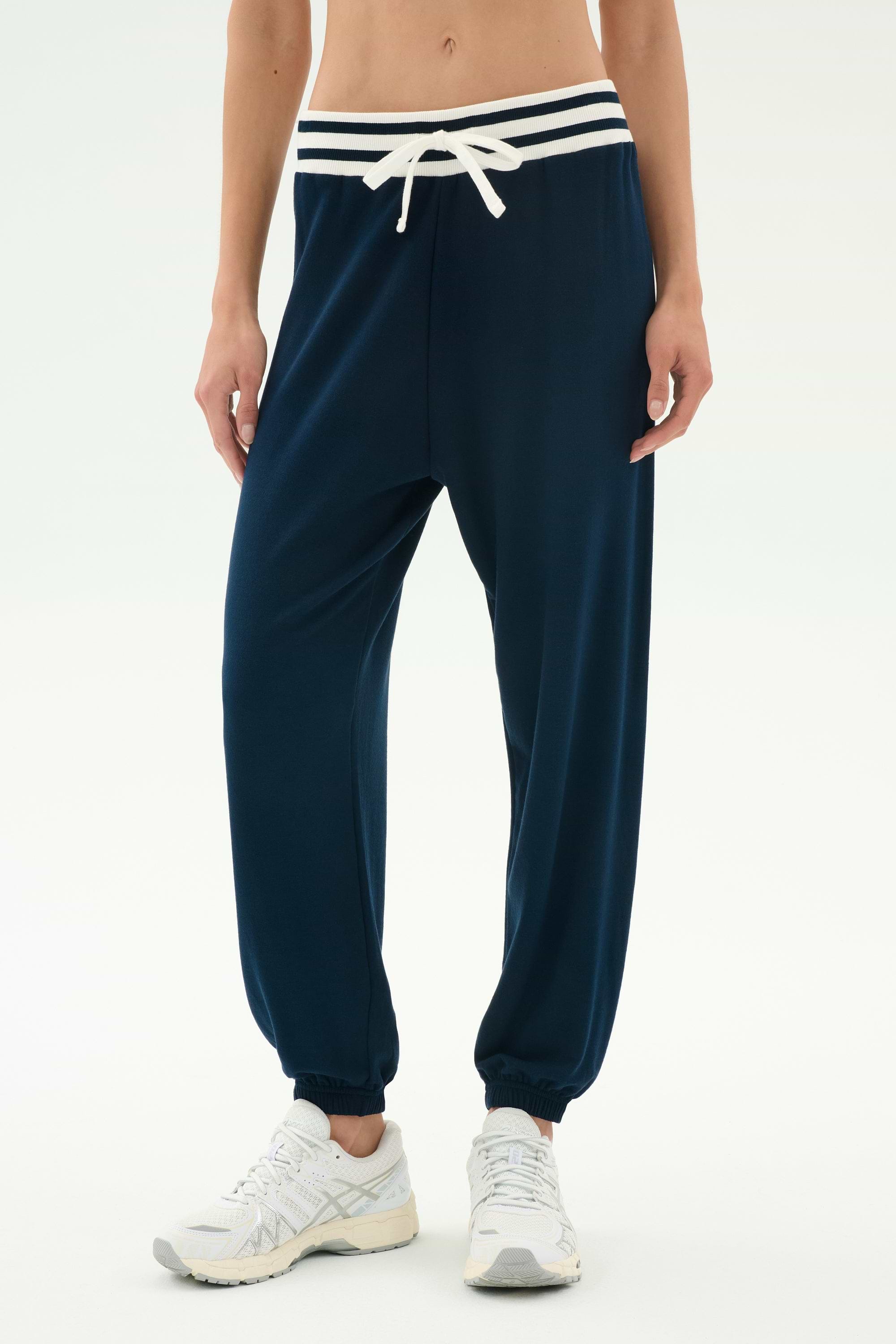 Model wears SPLITS59 Andie Oversized Fleece Sweatpant W/ Stripe in Indigo, featuring a white drawstring and striped waistband, paired with white sneakers against a plain light background.