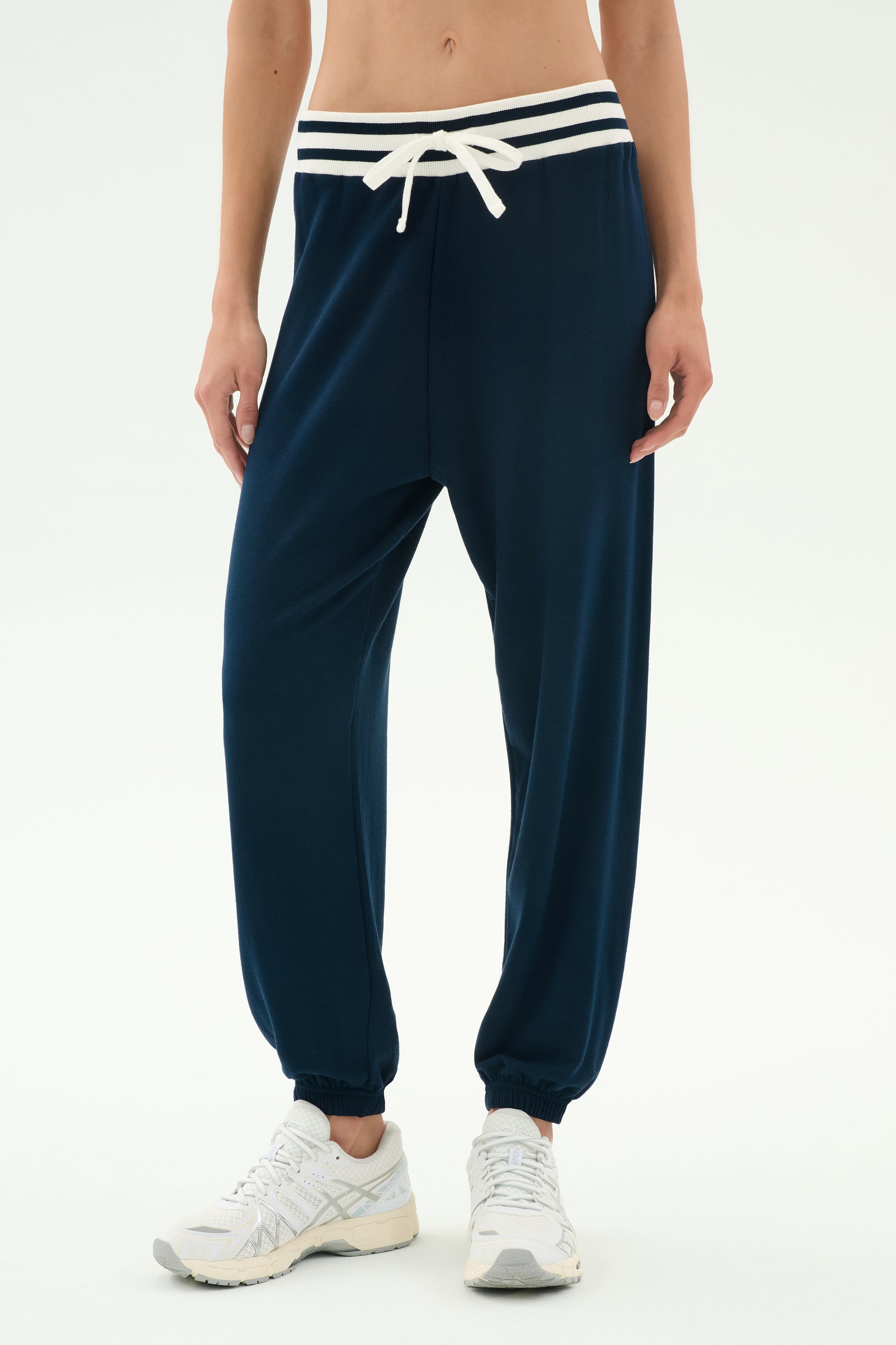 Model wears SPLITS59 Andie Oversized Fleece Sweatpant W/ Stripe in Indigo, featuring a white drawstring and striped waistband, paired with white sneakers against a plain light background.