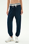 Model wears SPLITS59 Andie Oversized Fleece Sweatpant W/ Stripe in Indigo, featuring a white drawstring and striped waistband, paired with white sneakers against a plain light background.
