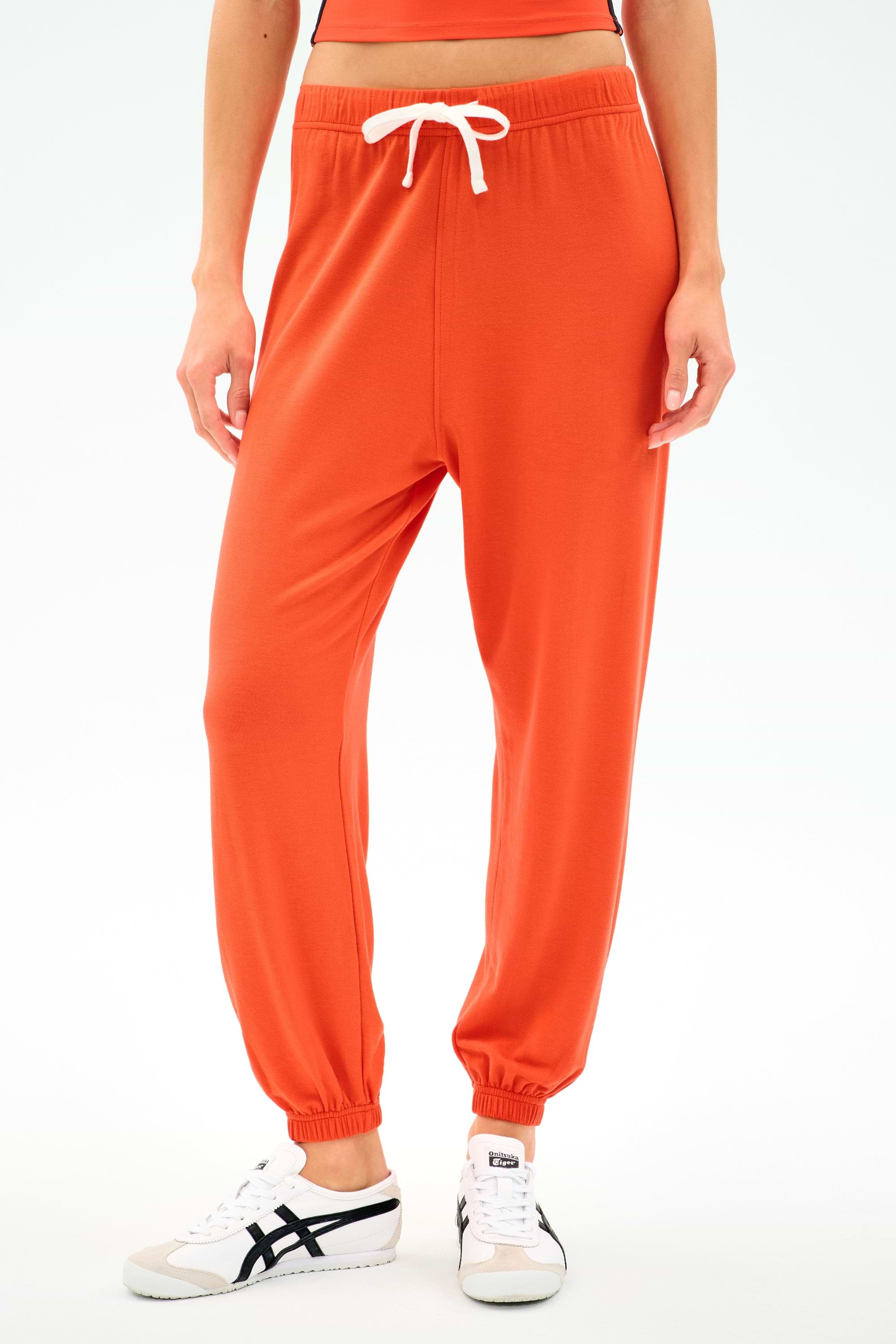 A person wears the SPLITS59 Andie Oversized Fleece Sweatpant in Valencia with a white drawstring and white sneakers, standing against a plain light background.
