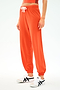 A person wearing SPLITS59's Andie Oversized Fleece Sweatpant in Valencia, an eye-catching orange, paired with white sneakers with black accents, stands against a plain light background.