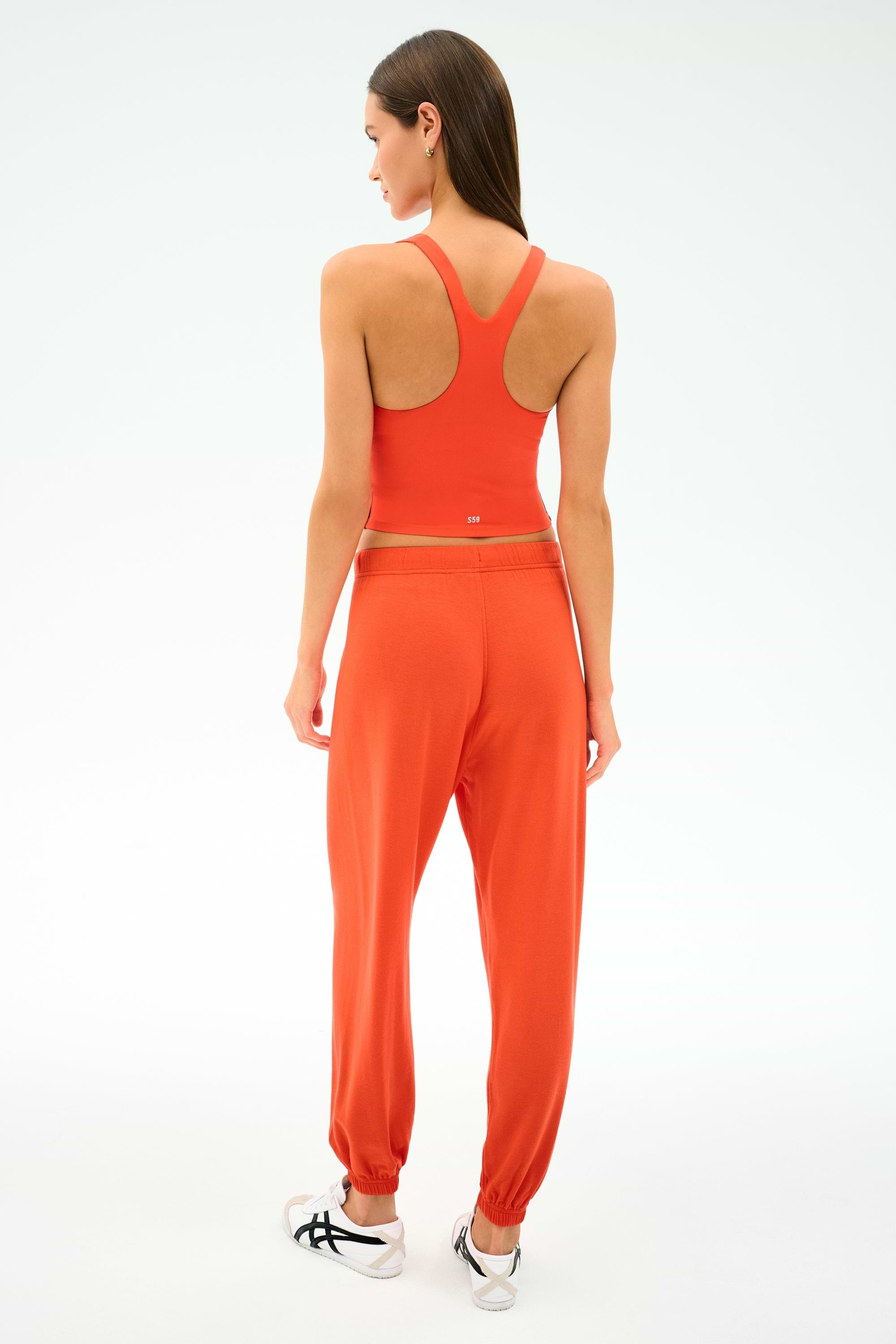 A woman stands with her back to the camera in the SPLITS59 Ella Airweight Tank in Valencia/Indigo, paired with matching stretch jogger pants and white sneakers, against a plain white background.