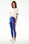 A woman wears the SPLITS59 Djuna Oversized Crop Jersey Tee - Creme/Cobalt, blue spandex leggings with a red side stripe, and white sneakers on a plain white background.