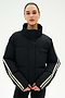 A person wearing the SPLITS59 Maeve Puffer Jacket in Black/Creme—crafted from 100% nylon and featuring white stripes on the sleeves—stands against a plain white background.