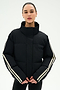 A person wearing the SPLITS59 Maeve Puffer Jacket in Black/Creme—crafted from 100% nylon and featuring white stripes on the sleeves—stands against a plain white background.
