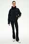 A person stands against a plain background wearing the SPLITS59 Maeve Puffer Jacket in Black/Creme, featuring 100% nylon construction and striped sleeves, paired with black pants and white sneakers with black stripes.