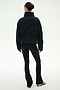 A person stands with their back to the camera, wearing the SPLITS59 Maeve Puffer Jacket in Black/Creme, paired with black flared leggings and black and white sneakers, set against a plain white background.
