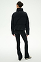 A person stands with their back to the camera, wearing the SPLITS59 Maeve Puffer Jacket in Black/Creme, paired with black flared leggings and black and white sneakers, set against a plain white background.