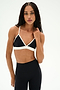 A person stands against a plain white background, wearing the SPLITS59 Sage Rigor Bra in Black/White and black nylon leggings, with long braided hair and a neutral facial expression.