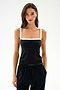 A woman stands against a plain background, wearing the SPLITS59 Monah Rigor Tank in Black/White—a sleeveless top featuring contrasting white straps and crafted from Rigor performance fabric—paired with black pants and one hand in her pocket. Ideal for gym sessions or casual wear.