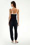 A woman stands with her back to the camera, wearing the SPLITS59 Monah Rigor Tank in Black/White, featuring a black body and contrasting white straps crafted from signature Rigor fabric. She pairs it with black pants and white slip-on shoes against a plain white backdrop. This versatile tank is ideal for both gym workouts and casual wear.