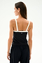 A woman with straight brown hair models the SPLITS59 Monah Rigor Tank in Black/White, featuring white straps and crafted from Rigor fabric. She pairs it with black pants and stands facing away from the camera against a plain white background.