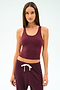 A woman stands against a plain light background wearing the SPLITS59 Ella Airweight Tank in Dark Cherry/Valencia, paired with matching sweatpants featuring a white drawstring, both crafted from stretchy nylon spandex fabric.