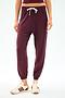 A person is wearing SPLITS59's Andie Oversized Fleece Sweatpant in Dk Cherry, styled with beige sneakers featuring maroon stripes, standing against a plain white background.