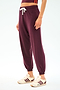 A person wears SPLITS59’s Andie Oversized Fleece Sweatpant in Dk Cherry with a white drawstring, paired with a cropped top and white sneakers featuring burgundy stripes, standing against a plain background.
