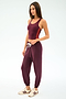 A woman wears the SPLITS59 Ella Airweight Tank in Dark Cherry/Valencia with matching jogger pants and white sneakers, standing against a plain light background.
