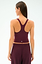 A woman with straight brown hair is seen from the back, wearing the SPLITS59 Ella Airweight Tank in Dark Cherry/Valencia, paired with matching pants, against a plain light background.