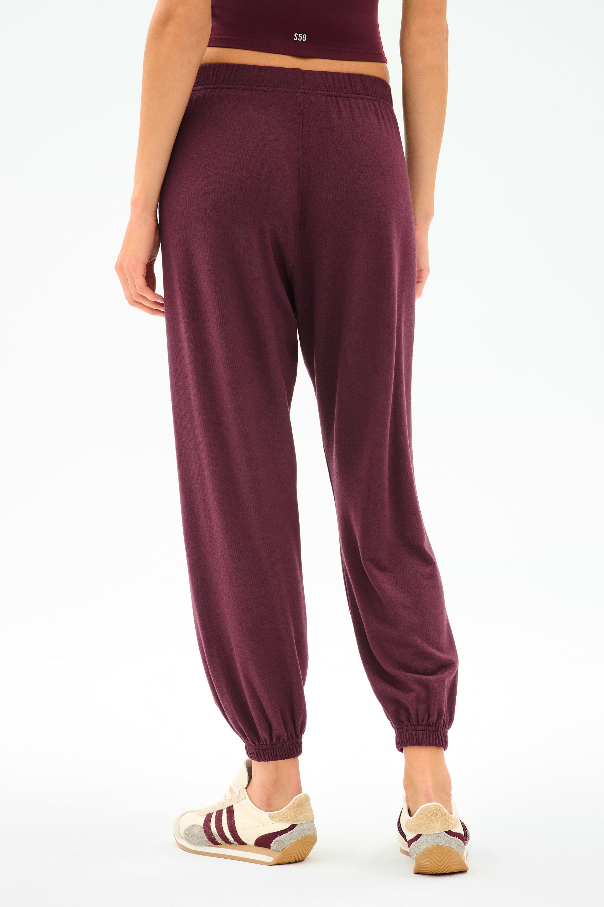 A person is seen from the back wearing SPLITS59 Andie Oversized Fleece Sweatpant in Dk Cherry and beige sneakers with maroon stripes, set against a plain white background.