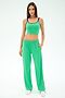 A woman faces forward wearing the SPLITS59 Cait Rigor Bralette in Grass/Indigo with matching green loose-fit pants and white sneakers, set against a plain white background.