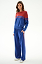 Woman wears the SPLITS59 Anna Knit Pullover - Cobalt/Terracotta with matching blue side-stripe pants and silver sneakers, posed against a plain white background.