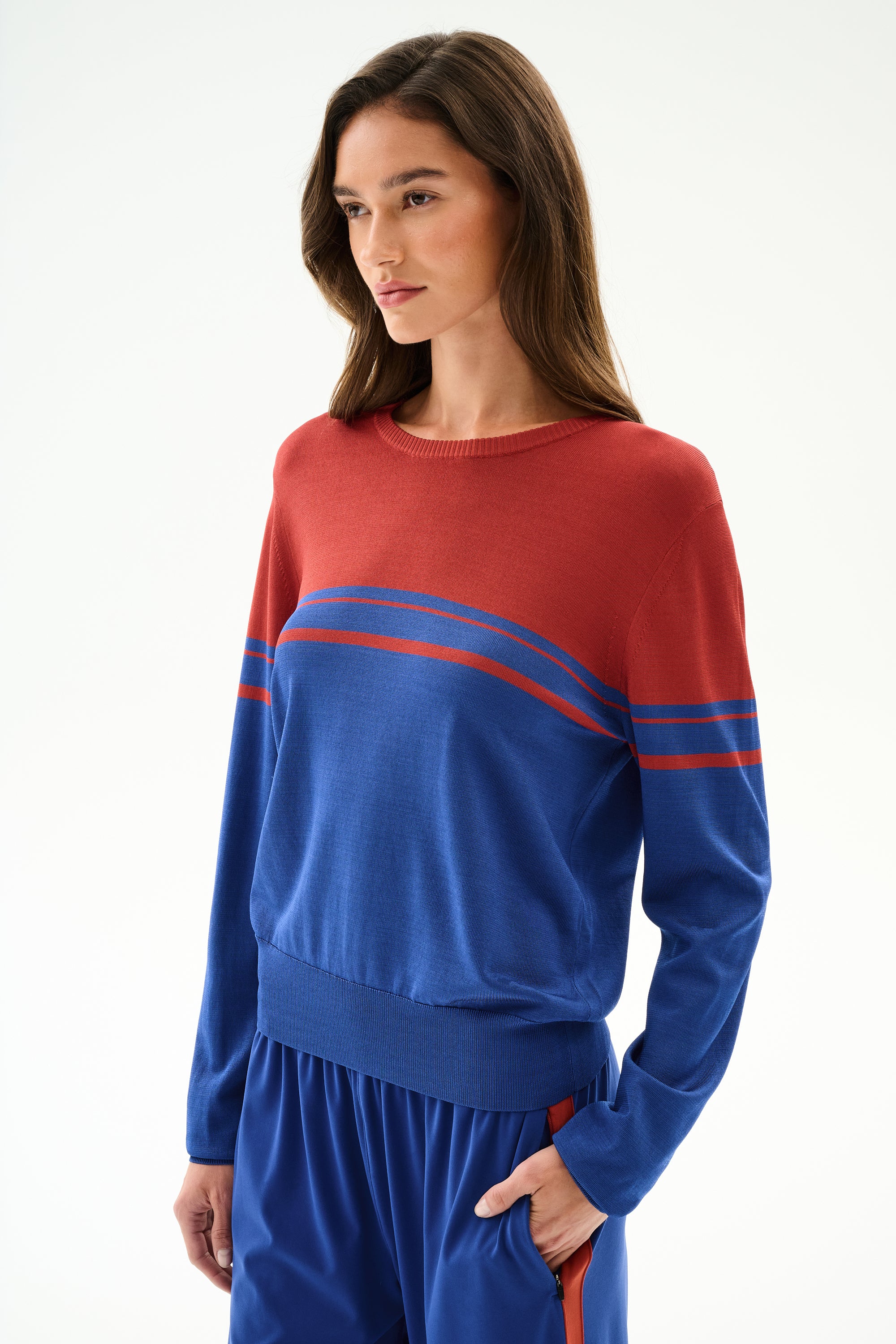Woman wears the SPLITS59 Anna Knit Pullover - Cobalt/Terracotta with blue pants, standing against a plain white background.
