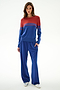 Woman stands against a white background in the SPLITS59 Anna Knit Pullover - Cobalt/Terracotta, blue wide-leg pants, and silver sneakers, left hand in her pocket.