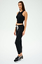 A person wearing the SPLITS59 Kiki Rib Crop Tank in black, paired with black joggers and sneakers, stands against a plain background, ready for gym workouts.