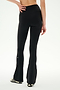 A person stands with one hand on their hip, shown from the back, wearing SPLITS59’s Raquel Crossover Supplex Flare leggings in black—featuring a flattering crossover waist and high-rise fit—paired with black-and-white sneakers against a plain white background; perfect for yoga sessions or comfortable everyday wear.