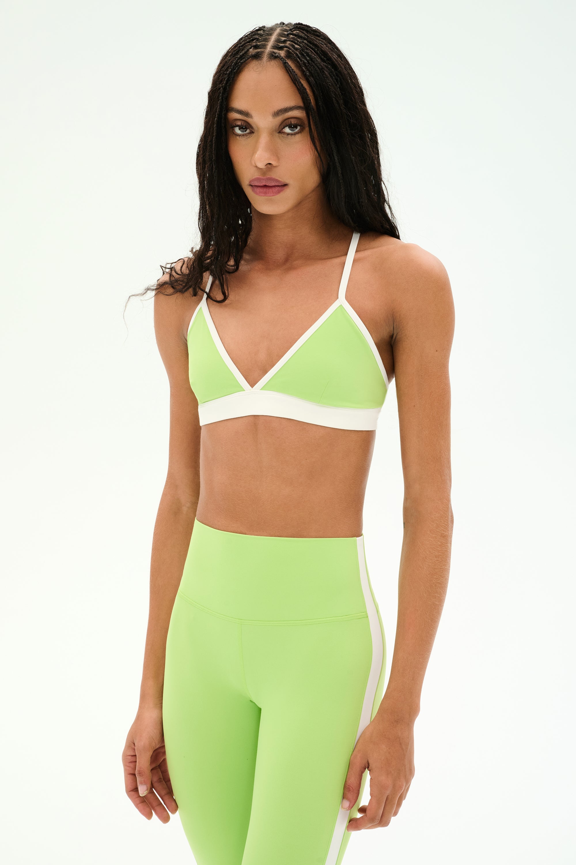 A person stands against a plain background, wearing the SPLITS59 Sage Rigor Bra in Limeade/White and matching high-waisted leggings, both crafted from a soft nylon-spandex blend.