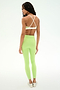 A woman stands on a white background, facing away from the camera, wearing the SPLITS59 Sage Rigor Bra in Limeade/White with crisscross straps and matching high-waisted leggings crafted from a smooth nylon-spandex blend, paired with white shoes.