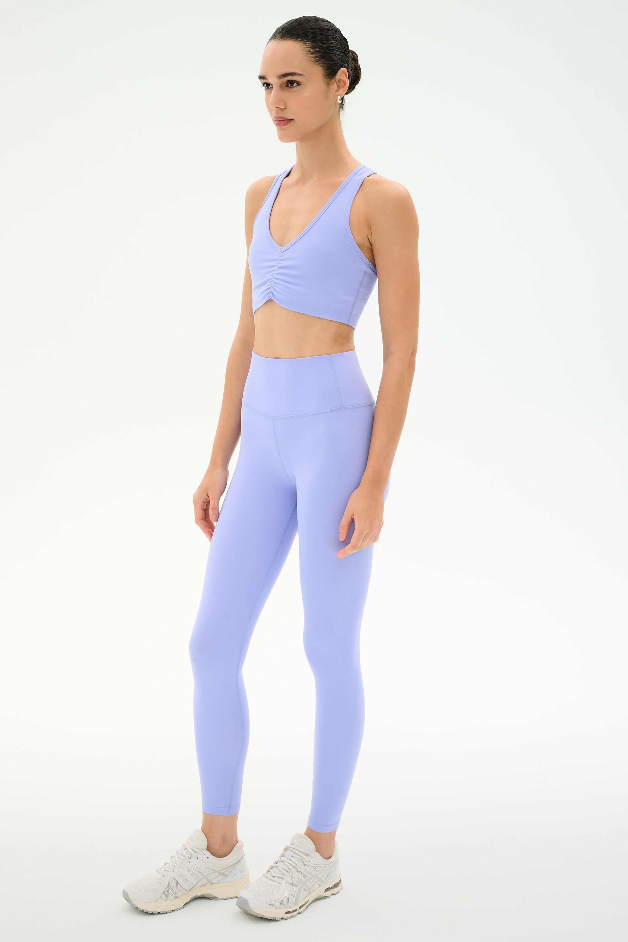 A woman models the SPLITS59 Airweight High Waist 26" leggings in Purple Haze—a light purple, stretchy sports bra and high-waisted legging set—standing against a plain white background, facing slightly to the side.