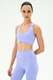 A person stands facing forward in a SPLITS59 Airweight Bra with Ruching in Purple Haze and matching high-waisted leggings, set against a plain white background.