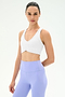 A person wears the SPLITS59 Airweight Bra with Ruching in white and high-waisted lavender leggings, standing against a plain light background.