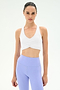 A woman models the SPLITS59 Airweight Bra with Ruching in white, paired with high-waisted pastel purple leggings, standing against a plain light background and looking directly at the camera.
