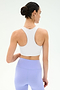 A woman with dark hair in a bun models the SPLITS59 Airweight Bra with Ruching in white, paired with high-waisted lavender leggings, shown from the back against a plain light background.