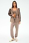A woman stands in the SPLITS59 Reggie Water Repellent Jacket in Latte/Black with matching joggers, a beige crop top, and white sneakers, set against a plain light background.