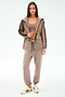 A woman stands in the SPLITS59 Reggie Water Repellent Jacket in Latte/Black with matching joggers, a beige crop top, and white sneakers, set against a plain light background.