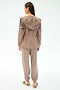 A woman stands with her back to the camera, wearing the SPLITS59 Reggie Water Repellent Jacket in Latte/Black, paired with matching casual pants and beige-maroon sneakers against a light background.