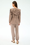 A woman stands with her back to the camera, wearing the SPLITS59 Reggie Water Repellent Jacket in Latte/Black, paired with matching casual pants and beige-maroon sneakers against a light background.