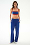 A woman stands facing forward in SPLITS59 Maxie Rigor Track Pant - Cobalt/Terracotta, paired with a blue and red sports bra and silver sneakers against a white background.