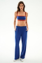 A woman stands facing forward in SPLITS59 Maxie Rigor Track Pant - Cobalt/Terracotta, paired with a blue and red sports bra and silver sneakers against a white background.