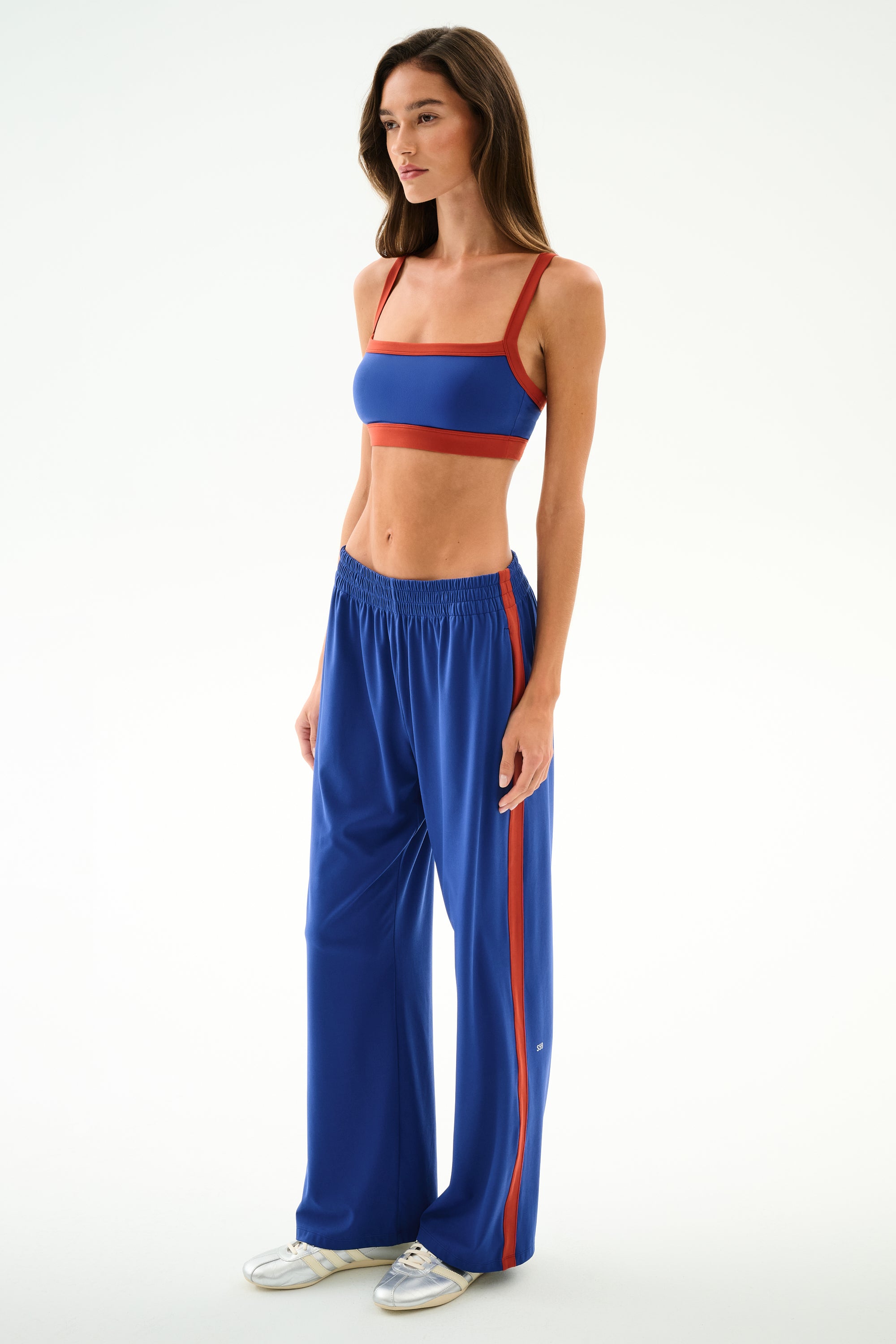 Woman wearing SPLITS59 Maxie Rigor Track Pant - Cobalt/Terracotta and a blue sports bra, standing against a plain white background.