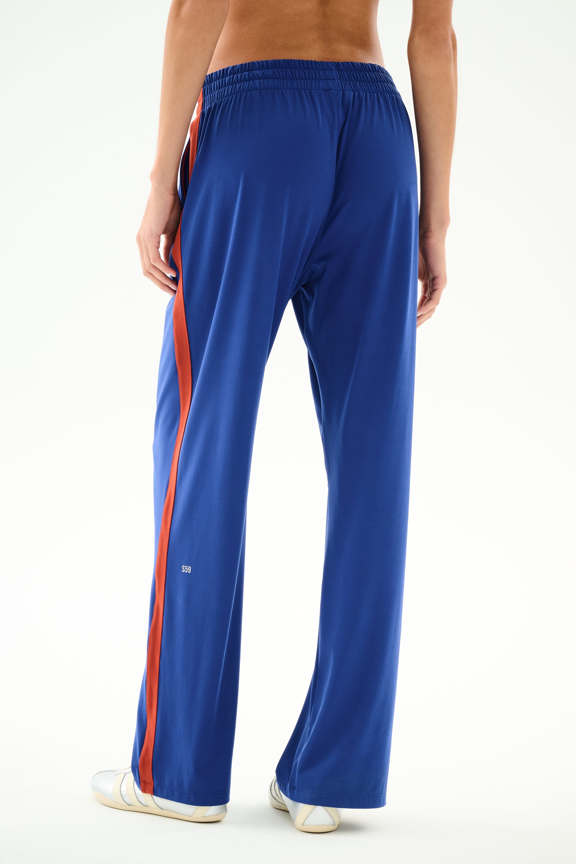 A person stands barefoot on a white background wearing SPLITS59 Maxie Rigor Track Pant - Cobalt/Terracotta, photographed from behind.