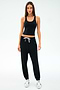 A woman faces forward in the SPLITS59 Ella Airweight Tank - Black/White, paired with black jogger pants and white sneakers, set against a plain white background.