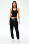 A woman faces forward in the SPLITS59 Ella Airweight Tank - Black/White, paired with black jogger pants and white sneakers, set against a plain white background.