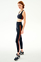 A person wearing an Ella Airweight Bra - Indigo/Valencia and high-waisted leggings in a stretch material, both featuring bright orange side stripes, paired with athletic sneakers.