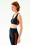 A dark blue Ella Airweight Bra - Indigo/Valencia with two vertical orange stripes on the side, worn with matching high-waisted leggings.