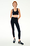 A person wearing a dark blue nylon sports bra and SPLITS59 Ella High Waist Airweight 7/8 - Indigo/Valencia leggings with orange side stripes, paired with dark blue running shoes.