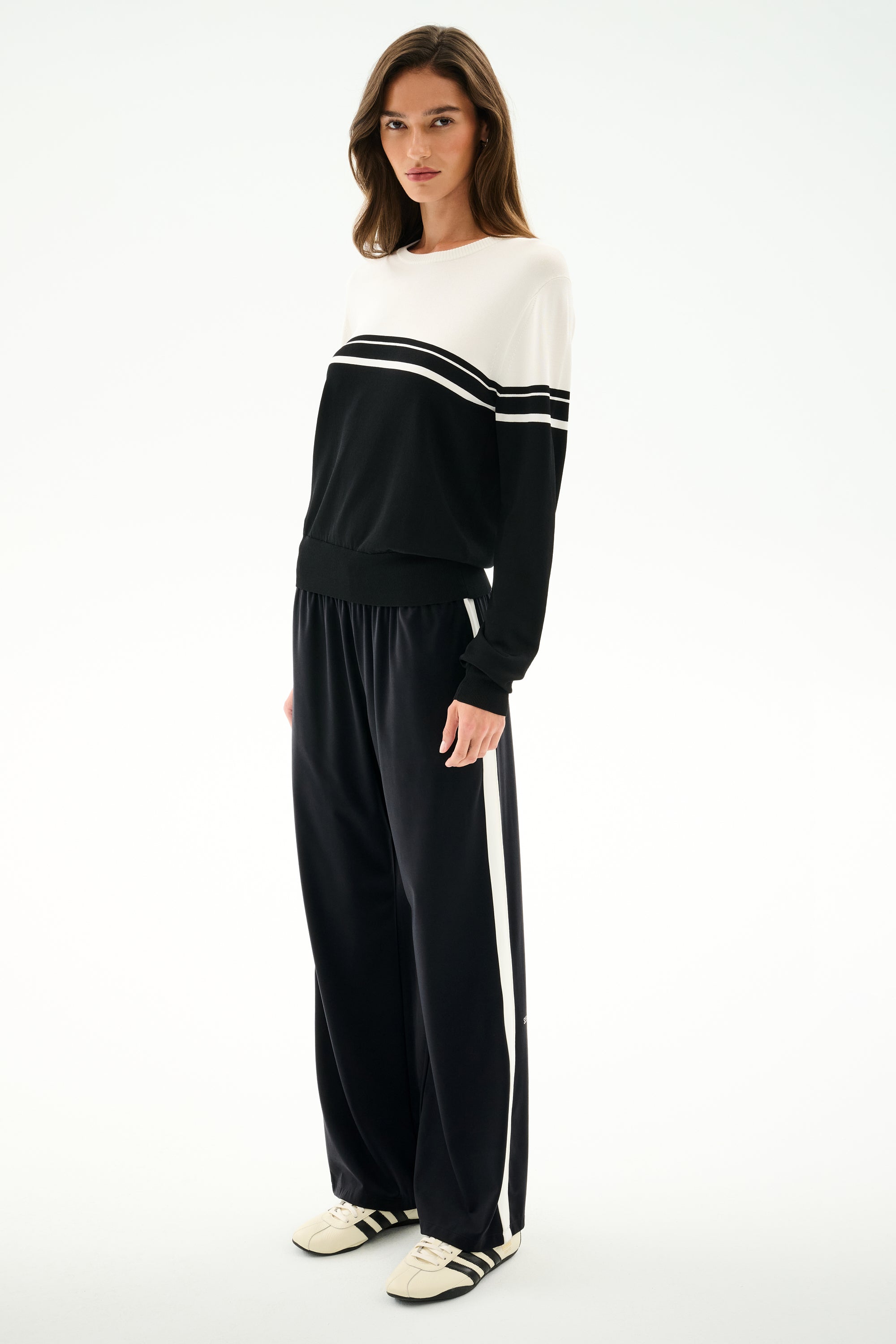 Woman wears the SPLITS59 Anna Knit Pullover - Black/White with matching wide-leg track pants and white sneakers, standing against a plain white background.